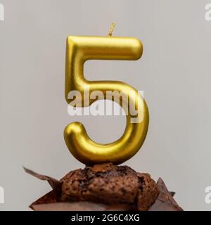 Bougie dorée en forme de cinq sur un muffin au chocolat sur fond gris Banque D'Images