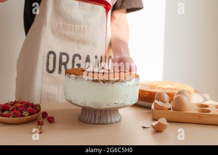 Male pastry chef pouring confiture ou sirop dans morceau de gâteau délicieux sur table en bois Banque D'Images