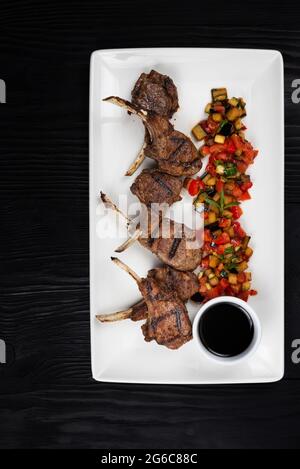 Côtes d'agneau grillées aux légumes sur palte blanc sur fond de bois noir Banque D'Images