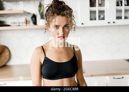 Jeune femme sportive restant seule dans la salle de séjour, regardant l'appareil photo, fille de taille sérieuse portant des vêtements de sport séance d'entraînement à la maison pour un style de vie sain de corps Banque D'Images