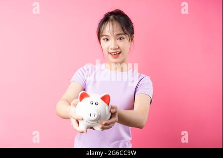 Portrait d'une fille tenant une banque de porc à la main, isolée sur fond rose Banque D'Images