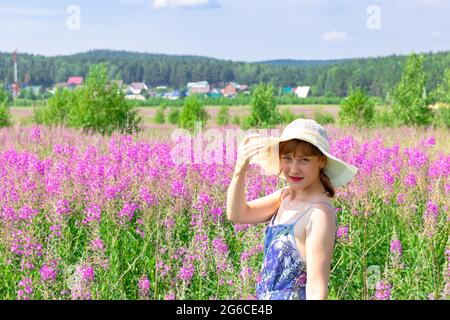 Jeune femme dans un champ de fleurs dans un chapeau de paille sur un fond de forêt verte et ciel bleu lors d'une chaude journée d'été. Mise au point sélective Banque D'Images