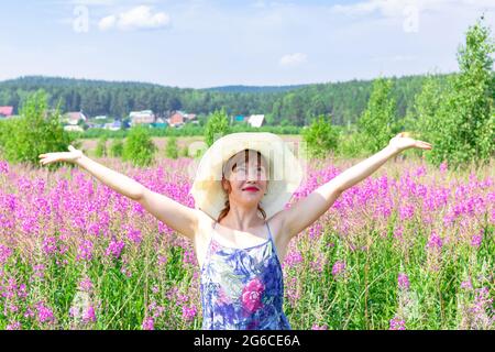 Jeune femme dans un champ de fleurs dans un chapeau de paille sur un fond de forêt verte et ciel bleu lors d'une chaude journée d'été. Mise au point sélective Banque D'Images