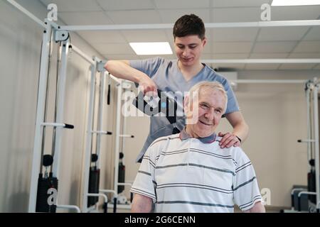 Thérapeute physique avec pistolet de massage musculaire traitant le patient Banque D'Images