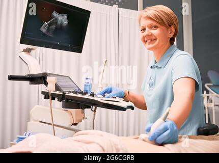 Femme échographiste examinant un patient à l'aide d'un échographe. Médecin souriant lors de l'examen échographique dans une armoire gynécologique. Concept de santé, d'échographie et de diagnostic échographique. Banque D'Images