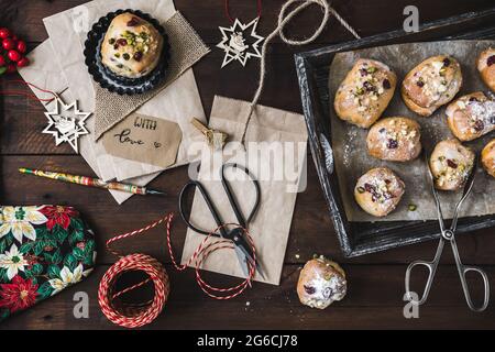 Scène de cadeaux à l'Avent avec mini-Stollen, sacs en papier, ciseaux, porte-stylo et ruban cadeau sur bois sombre Banque D'Images