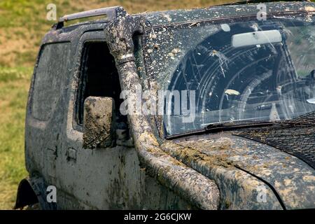 une voiture sale recouverte d'une couche de pulvérisation de marécages à la suite de la conduite hors route par temps ensoleillé, les essuie-glaces balaient le pare-brise du marécage Banque D'Images