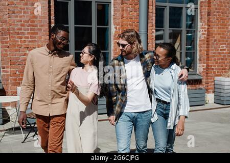 Portrait de jeunes gens modernes qui marchent dans la rue de la ville éclairée par la lumière du soleil, tous portant des lunettes de soleil Banque D'Images