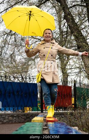 Des femmes plus âgées heureuses qui s'amusent à l'extérieur. Senior gai mature mature femme à la retraite avec parapluie jaune profitant de la vie au jour de pluie dans le parc. Plaisir Banque D'Images