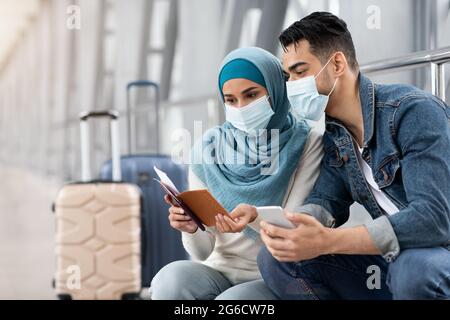 Couple musulman en masques médicaux attendant un vol dans le terminal de l'aéroport Banque D'Images