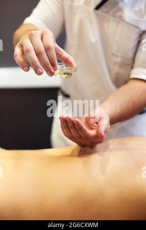 Une masseuse sans visage qui verse de l'huile à la main pendant un massage relaxant dans le centre de spa Banque D'Images