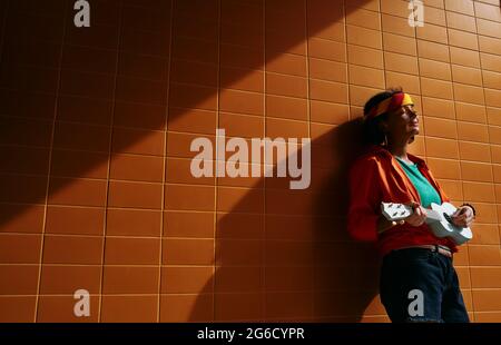 Jeune femme au look coloré jouant ukulele penché contre le mur urbain debout dans les rayons du coucher du soleil avec de longues ombres Banque D'Images