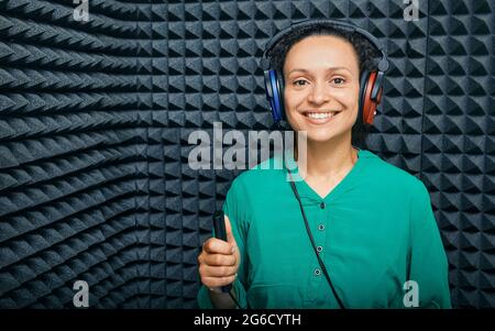 Portrait d'une femme adulte pendant l'audition de l'enregistrement dans une cabine audiométrique insonorisée à l'aide d'un casque audiométrique et d'un audiomètre Banque D'Images