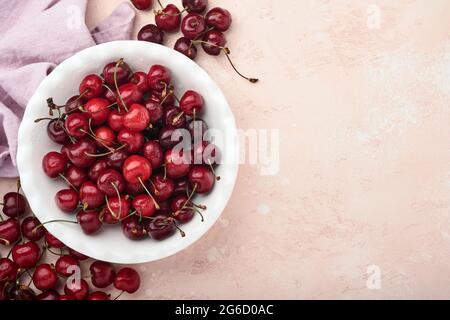 Cerise avec gouttes d'eau sur un bol blanc sur une table en pierre rose. Cerises fraîches et mûres. Cerises rouges sucrées. Vue de dessus. Style rustique. Fond de fruit Banque D'Images