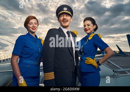 Aviateur et agents de bord joyeux debout sur les escaliers d'embarquement Banque D'Images