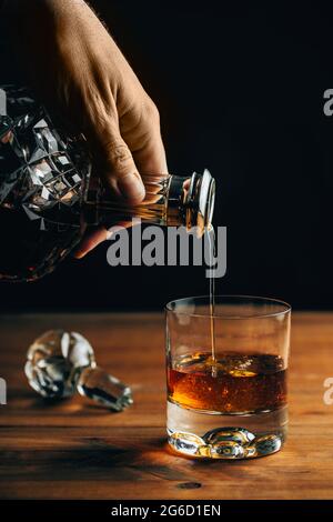 Verre de whisky froid avec glace placé sur une table en bois près du décanter sur fond noir Banque D'Images