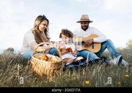 Nous avons ravi toute la famille multiraciale en dégustant un pique-nique ensemble tout en dégustant des en-cas et en jouant de la guitare dans la nature Banque D'Images