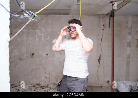 Un jeune constructeur met des lunettes de sécurité sur un chantier de construction. Homme portant des lunettes de protection. Banque D'Images