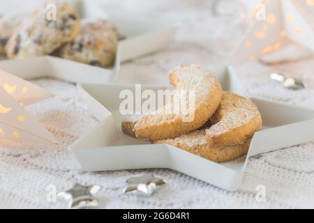 Biscuits croissant à la vanille sur une assiette d'étoiles blanches sur une couverture blanche, décorée avec des étoiles argentées et des étoiles, mini stollen en arrière-plan, s Banque D'Images