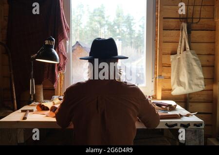 Vue arrière d'un homme en chapeau assis à la table et travaillant en atelier Banque D'Images