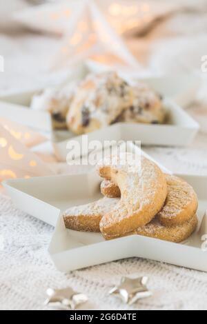 Biscuits à la vanille et mini-stollen sur des assiettes d'étoiles blanches sur une couverture blanche, décorée avec des étoiles argentées et des étoiles, mini-stollen en arrière-plan, Banque D'Images