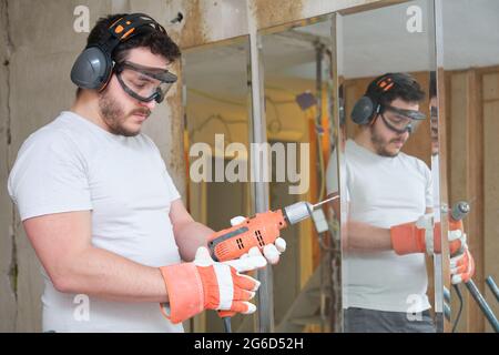 Le constructeur change un foret sur le chantier de construction. Travailleur de la construction portant des gants de sécurité, des lunettes et des couvre-oreilles. Banque D'Images