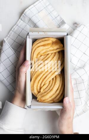 Vue de dessus de la femme sans visage à la table avec de la pâte crue préparée pour le dessert Babka et placée dans un plat de cuisson en métal Banque D'Images