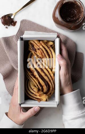 Vue de dessus de la femme sans visage à la table avec de la pâte crue préparée pour le dessert Babka et placée dans un plat de cuisson en métal Banque D'Images