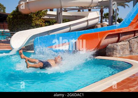 Antalya, Turquie-juin 30, 2021: Homme descendant sur le toboggan d'eau et entrant dans la piscine avec de grandes éclaboussures à l'aqua parc en vacances d'été. Banque D'Images