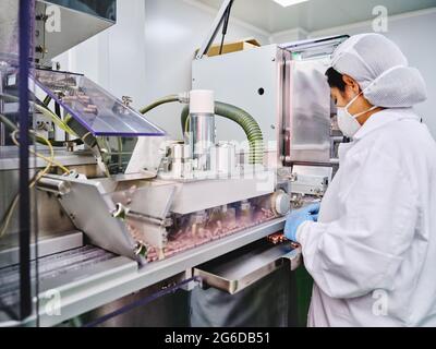 Vue latérale d'une travailleuse d'usine dans un convoyeur uniforme avec des pilules dans un laboratoire de fabrication pharmaceutique Banque D'Images