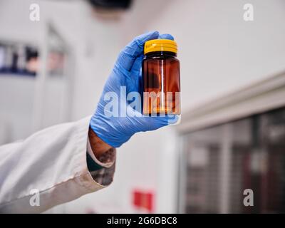 Crop anonyme scientifique dans des gants de protection debout montrant pile de capsules sur la bouteille en laboratoire Banque D'Images