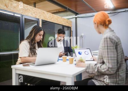 Groupe de collègues concentrés assis à table et travaillant ensemble sur le projet de démarrage dans l'espace de travail des collègues Banque D'Images