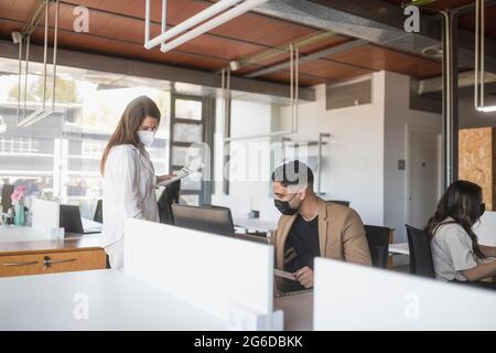 Des collègues hommes et femmes travaillant dans des masques de protection sur le projet dans un lieu de travail spacieux Banque D'Images