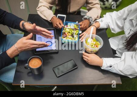 Par-dessus les collègues multiraciaux non reconnaissables et rognés assis à table et déjeunant pendant la pause au bureau Banque D'Images