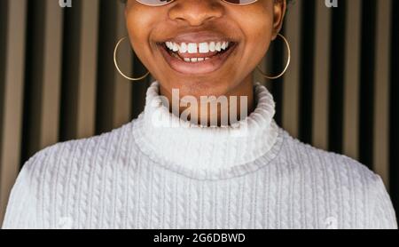 Crop Afro-américaines avec des dents gercées dans un chandail tendance souriant heureusement contre le mur rayé dans la rue Banque D'Images