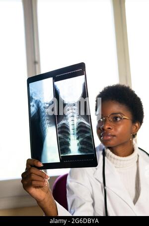 Jeune femme noire médique debout près de la fenêtre et examinant l'acquisition de rayons X pendant le travail en clinique Banque D'Images