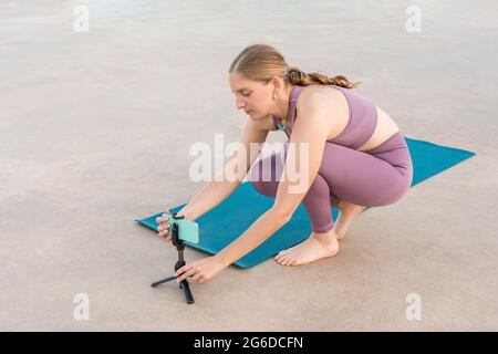 Angle élevé de femme préparant téléphone mobile sur trépied pour faire du yoga pendant la leçon en ligne Banque D'Images