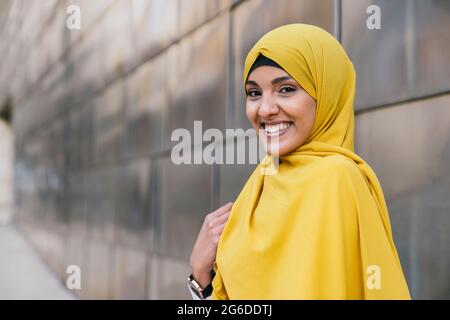 Femme musulmane branchée dans hijab jaune debout dans la rue et regardant la caméra Banque D'Images