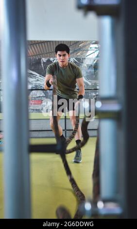 Entraînement d'homme asiatique concentré avec corde de combat dans un gymnase crossfit moderne Banque D'Images