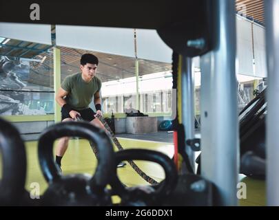 Entraînement d'homme asiatique concentré avec corde de combat dans un gymnase crossfit moderne Banque D'Images