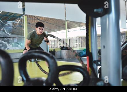 Entraînement d'homme asiatique concentré avec corde de combat dans un gymnase crossfit moderne Banque D'Images