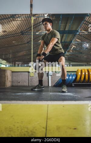 Homme asiatique s'entraîner sur les épaules et les bras avec de lourdes kettlebells dans la salle de gym pendant l'entraînement fonctionnel et regarder loin Banque D'Images