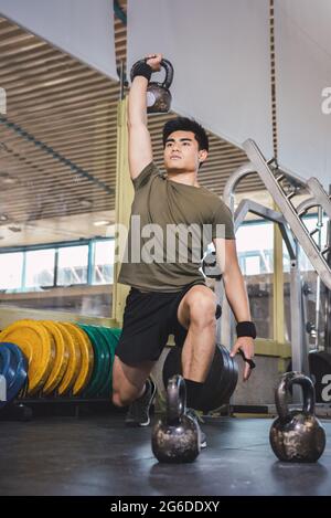 Homme asiatique s'entraîner sur les épaules et les bras avec de lourdes kettlebells dans la salle de gym pendant l'entraînement fonctionnel et regarder loin Banque D'Images