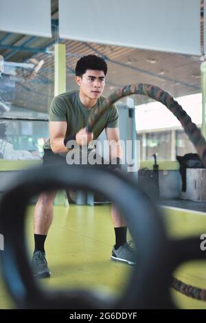Entraînement d'homme asiatique concentré avec corde de combat dans un gymnase crossfit moderne Banque D'Images