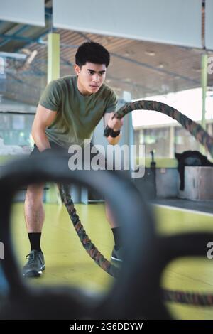 Entraînement d'homme asiatique concentré avec corde de combat dans un gymnase crossfit moderne Banque D'Images