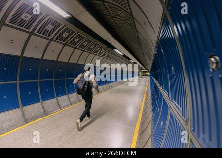 Vue arrière de l'homme anonyme avec sac à dos fonctionnant dans un tunnel vide de métro avec des murs bleus Banque D'Images