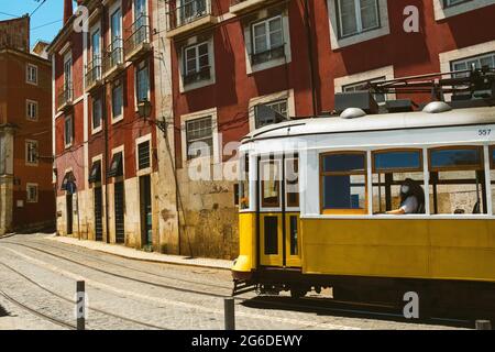 Tramway traditionnel jaune vintage avec femme à l'intérieur dans la rue à Lisbonne, Portugal dans une petite allée avec des bâtiments rouges. Destination de voyage célèbre Banque D'Images