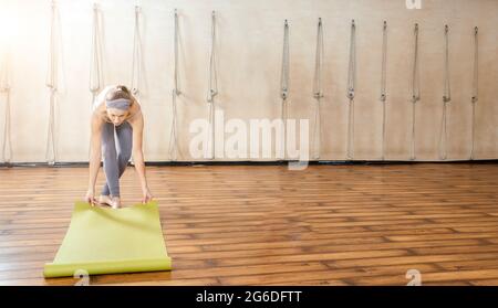 Jeune femme roulant tapis de yoga dans le studio de yoga avant le cours de formation. Copier l'espace Banque D'Images