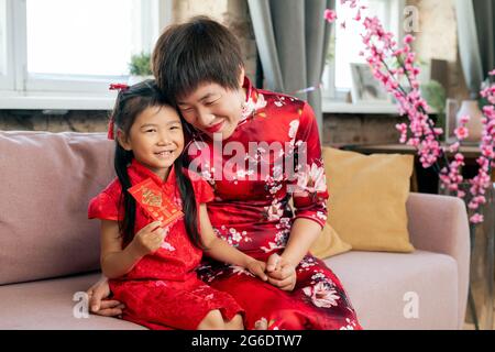 Bonne femme chinoise embrassant sa petite fille avec une carte postale du nouvel an Banque D'Images