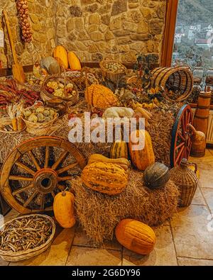 Citrouilles, maïs, pois, oignons, pommes, poires, poivrons, panier de fruits dans le foin avec une roue pour fauteuil roulant sur un mur en pierre Banque D'Images